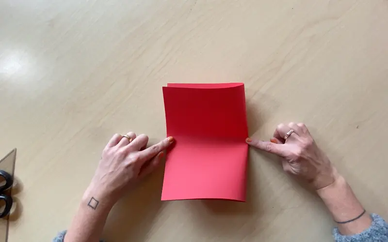 Hands pressing a clean center crease along a sheet of red cardstock
