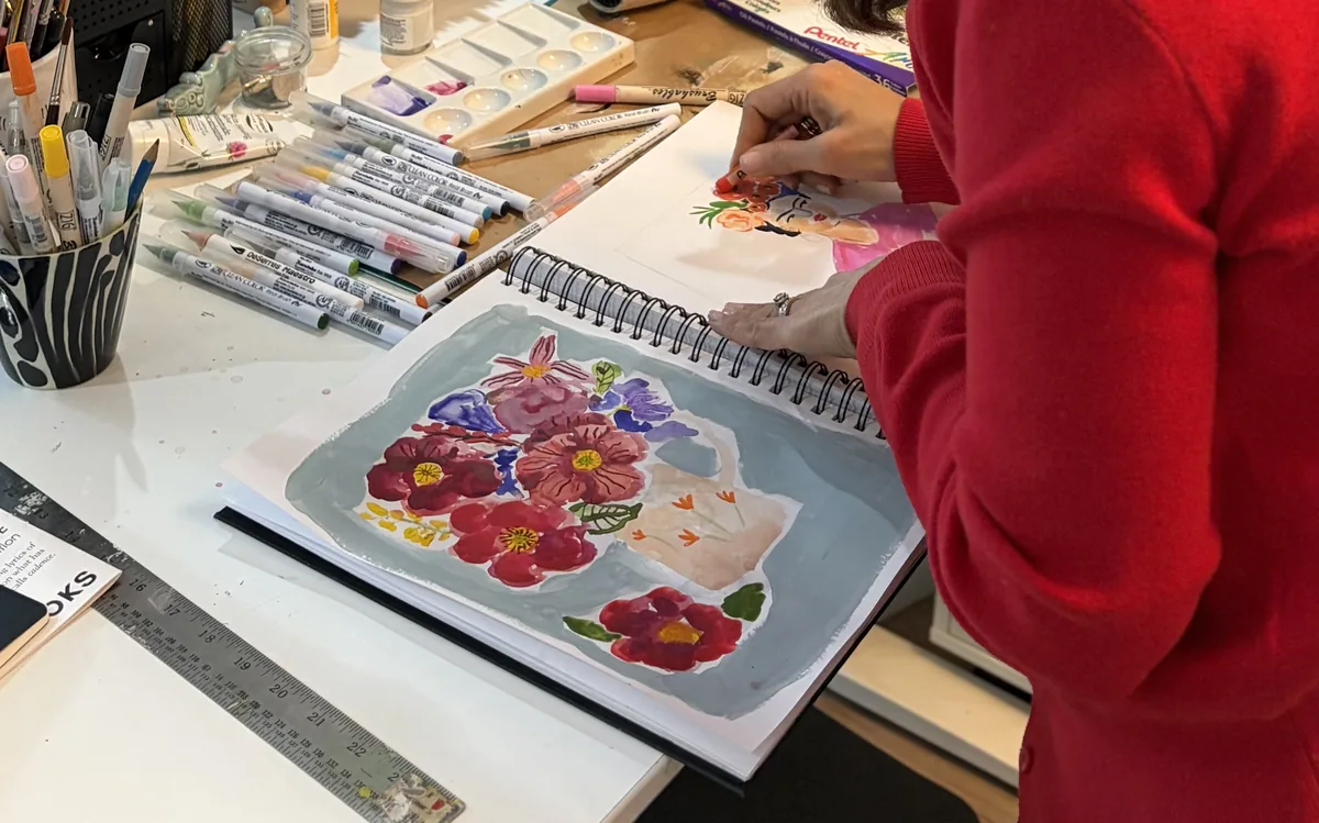 aras-summer-floral-motif-rom-2026 Artist painting a colourful floral bouquet in a spiral sketchbook
