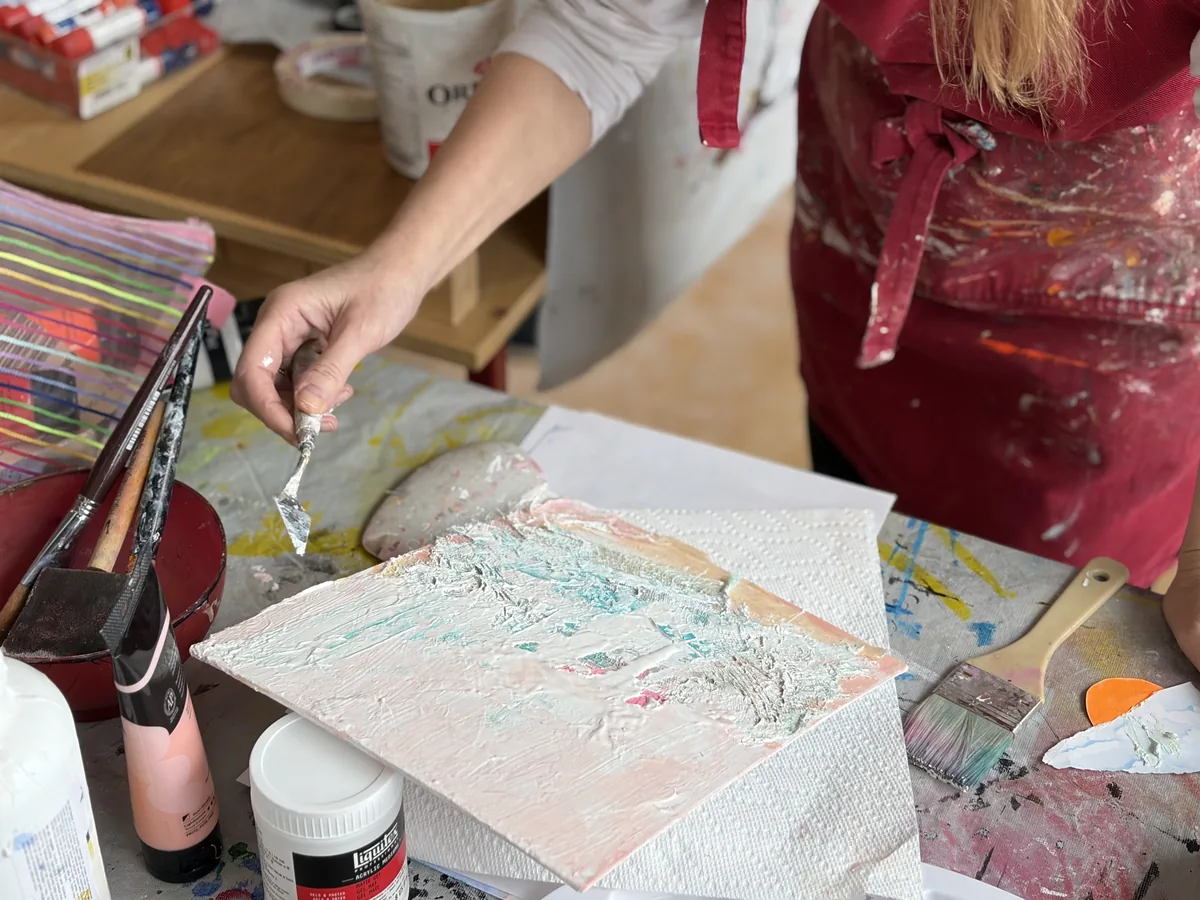 aras-summer-nature-in-abstraction-2026 Artist applying thick impasto paint to a small canvas with a palette knife in a studio setting